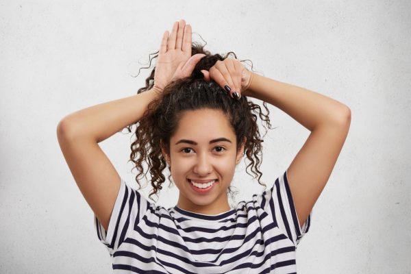 funny-female-model-has-crisp-hair-foolishes-alone-pretends-be-small-rabbit-kitten-makes-ears-with-hands (1)